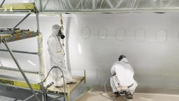Maler in Schutzanzügen lackieren Flugzeug