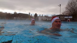 Zwei Menschen mit Weihnachtsmützen schwimmen im Freibad