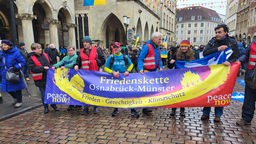 Eine Gruppe Menschen mit einem Transparent zur Friedenskette auf dem Prinzipalmarkt in Münster. 
