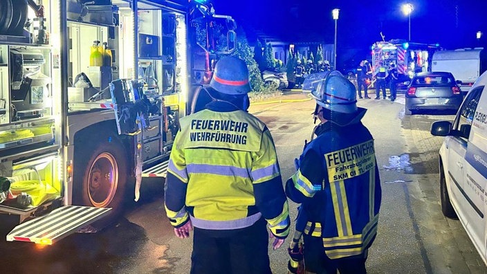 Zwei Feuerwehrkräfte von hinten neben einem Feuerwehrauto