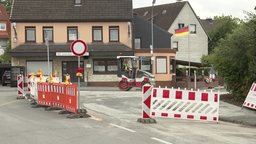 Rot-Weiße Baustellenabsperrungen. Im Hintergrund fährt eine Dampfwalze.