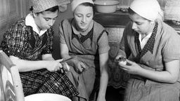Drei Frauen in einer Küche, die Kartoffeln schälen.
