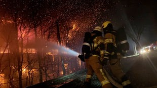 Zwei Feuerwehrleute lösche eine brennende Lagerhalle 