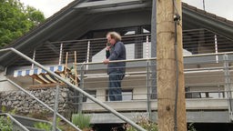 Ein Mann steht mit seinem Handy auf einem Balkon. 