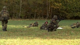 Soldaten liegend und hockend mit Gewehren auf einer Wiese