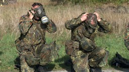 Zwei Soldaten setzen sich Gasmasken auf