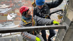 zwei Personen die im Klettergeschirr an dem Lamberti-Kirchtum hängen