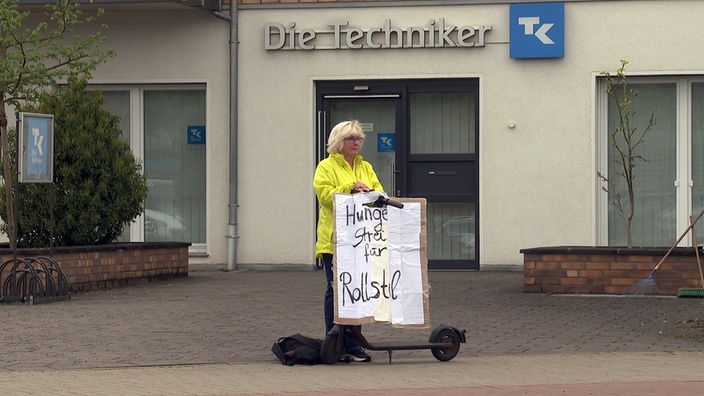 Sylvia Stütz hält ein Plakat mit der Aufschrift: "Hungerstreik für Rollstuhl" 
