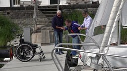 Männer helfen einem Rollstuhlfahrer beim Einsteigen