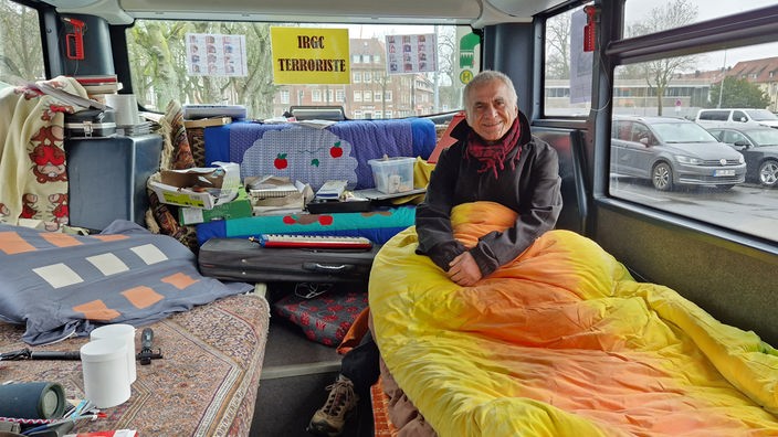 Fari Hadipour sitzt mit gelbem Schlafsack in einem Bus
