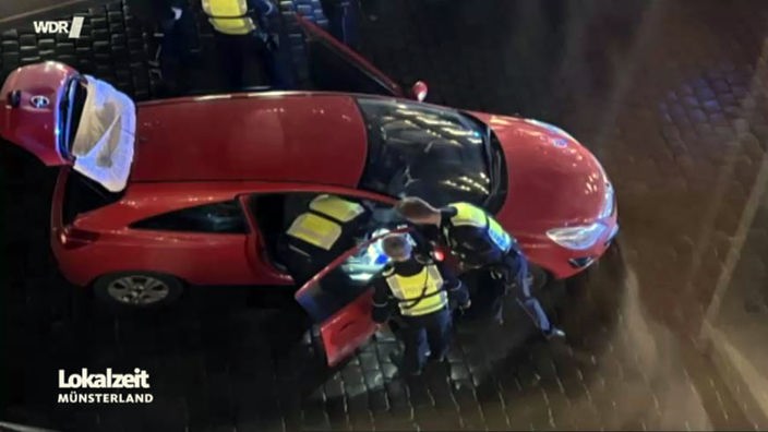 Rotes Auto mit offenen Türen wird von Polizisten untersucht.