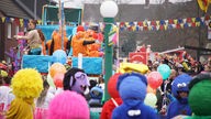 Ein Karnevalswagen mit orange kostümierten Jecken fährt am Nelkendienstag durch Olfen, viele kostümierte Besucherinnen und Besucherinnen stehen am Straßenrand.