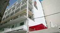 Ein mehrstöckiges weißes Hotelgebäude mit Balkonen und einer daneben liegenden Terasse mit einem roten Pavillon 