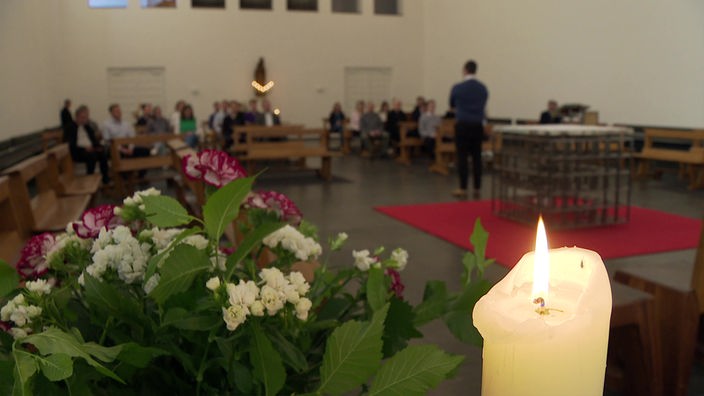Kapelle des Priesterseminars mit Betenden, im Vordergrund sind Blumen und eine Kerze aufgestellt.