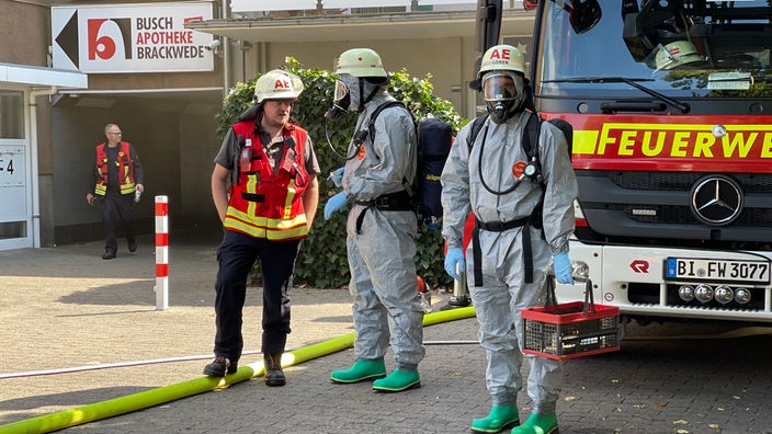 Feuerwehrkräfte stehen mit Atemschutzmaske vor einem Gebäude