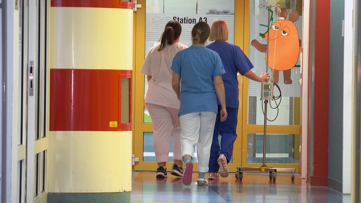 Drei Krankenschwestern laufen den Flur entlang in der Klinik. 