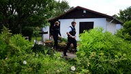 Zwei Polizeileute laufen vor der verdächtigen Gartenlaube her. 