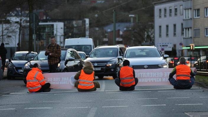 Vier Menschen sitzen auf der Straße und behindern den Verkehr