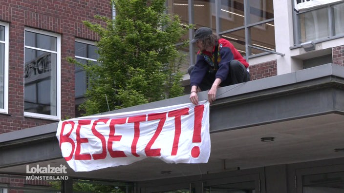 Ein Student hängt einen Banner mit der Aufschrift "Besetzt!" auf.