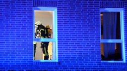 Ein Feuerwehrmann ist von außen hinter einem Fenster des Wohnhauses zu sehen. 