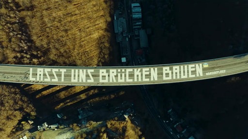 Eine Drohnenaufnahme der Brücke, die mit dem Spruch "Lasst uns eine Brücke bauen" bamalt ist