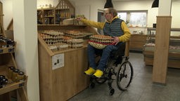 Ein querschnittgelähmter Mann im Rollstuhl sortiert Eier in Kartons ein.