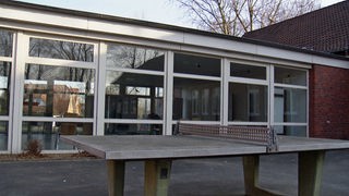 Tischtennisplatte vor einem leeren Schulgebäude.