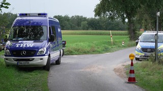 Auf dem Foto sind ein Einsatzfahrzeug des THW und der Polizein auf einem Feldweg zu sehen