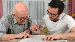 Junger Mann hilft altem Mann beim Ausfüllen eines Formulars