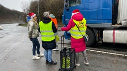 Vier Frauen mit gelben Warnwesten auf Nikolausmützen auf dem Kopf vor einem Lkw