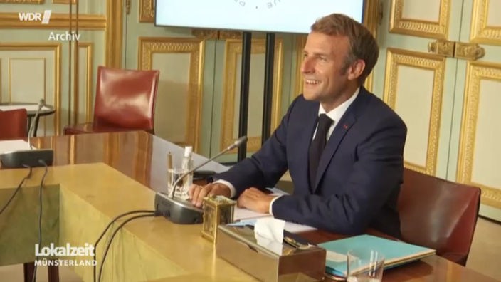 Der französische Präsident Macron sitzt an einem Tisch vor einem Mikrofon