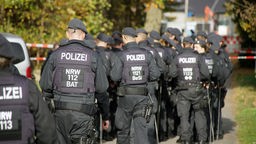 Viele Polizisten und Polizistinnen laufen in Uniform auf ein Absperrband zu.