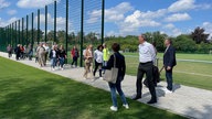 Eine Menschengruppe läuft über einen Weg, daneben ein Fußballplatz