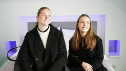 Zwei Studentinnen aus den Niederlanden sitzen auf einem Hotelbett und erfreuen sich an der einstellbaren Lichtfarbe des Zimmers