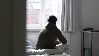Flüchtling Mohamed sitzt auf einem Bett und blickt aus dem Fenster