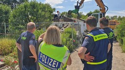 Polizeibeamte in einer Kleingartenanlage beobachten den Abriss einer Gartenlaube