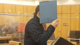 Ein Mann im Gericht hält sich einen Umschlag vors Gesicht