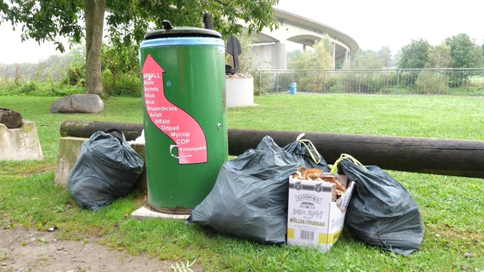 Mülltüten stehen neben einer grünen Mülltonne.