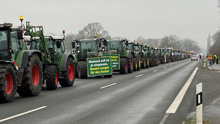 Man sieht einen langen Konvoi von Traktoren auf einer Landstraße.