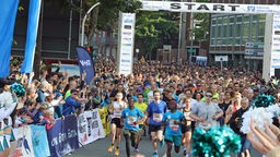 Hunderte Läufer, die durch ein Start-Tor laufen, und jubelnde Zuschauer