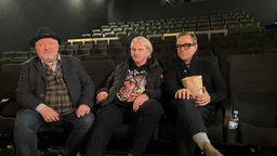 Schauspielkollegen Axel Prahl, Detlev Buck und Jan Josef Liefers sitzen im Kino 