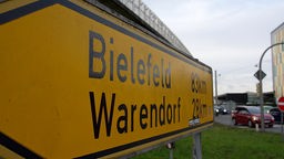 Ein gelbes Verkehrsschild, auf dem die Entfernungen nach Bielefeld und Warendorf stehen