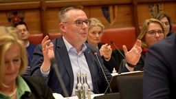 Stefan Weber von der CDU Münster sitzt im Rat neben seinen Kolleginnen und Kollegen und hebt die Hände hoch