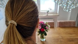 Frau von hinten zu sehen, auf dem Tisch steht ein Blumenstrauß in einer Vase. 