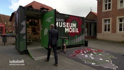 Ein Mann gehtr in einen Container mit der Aufschrift "MuseumMobil". 