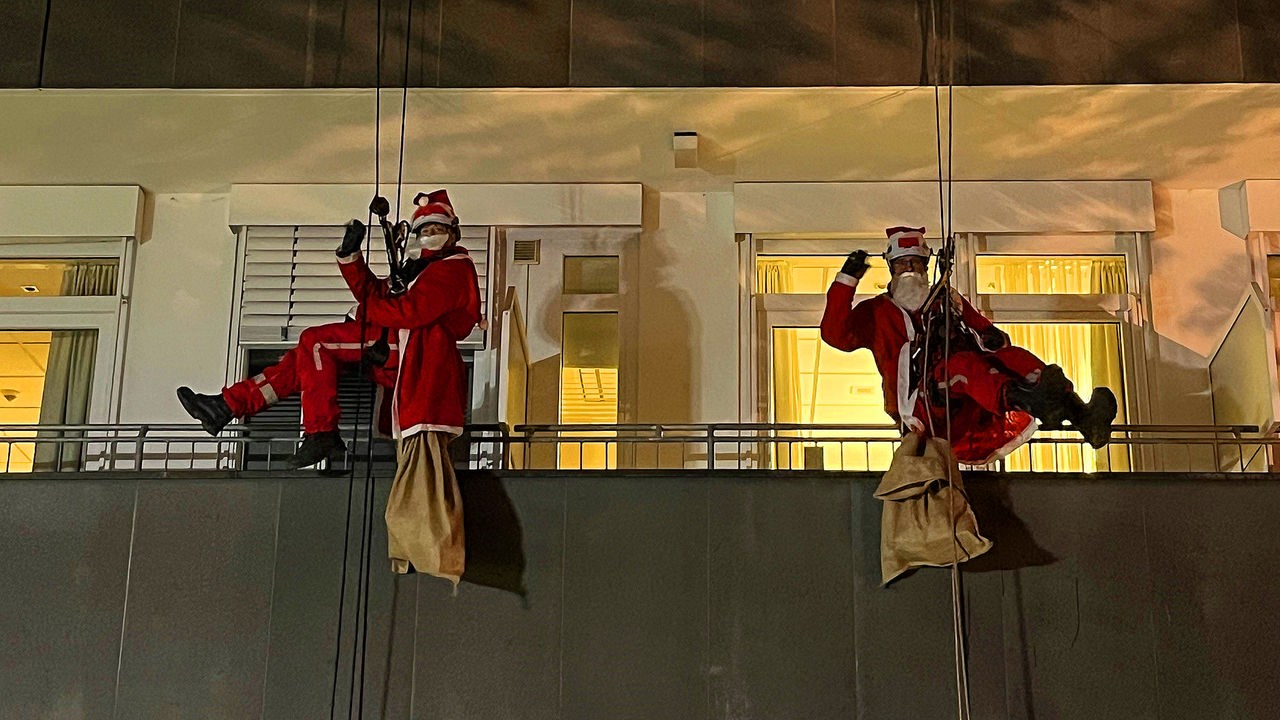 Zwei Menschen in Nikolaus-Kostüm seilen sich an einer Hauswand ab. 