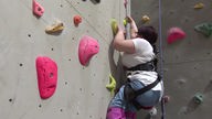 Eine Frau mit Behinderung klettert an der Kletterwand