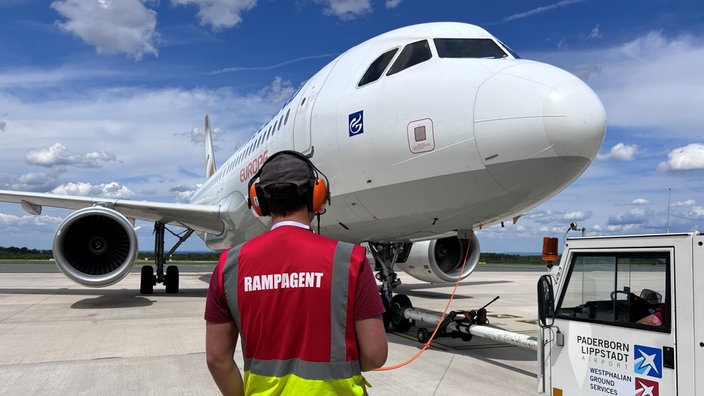 Ein Flughafenmitarbeiter steht vor einem geparktem Ferienflieger nach Rhodos.