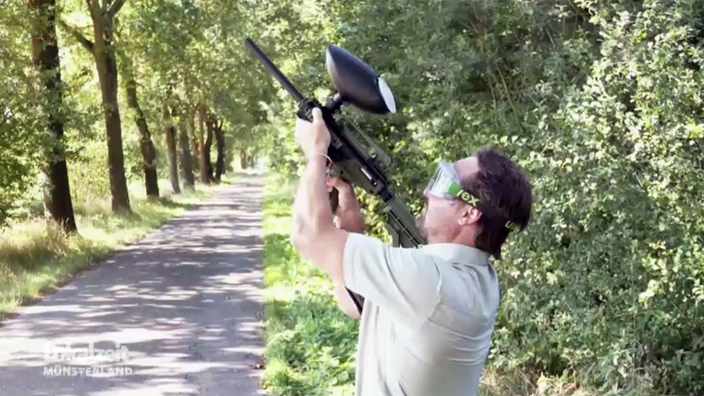 Ein Mitarbeiter vom Team Wald- und Klimaschutz schießt mit einer Paintballpistole auf einen Baum.