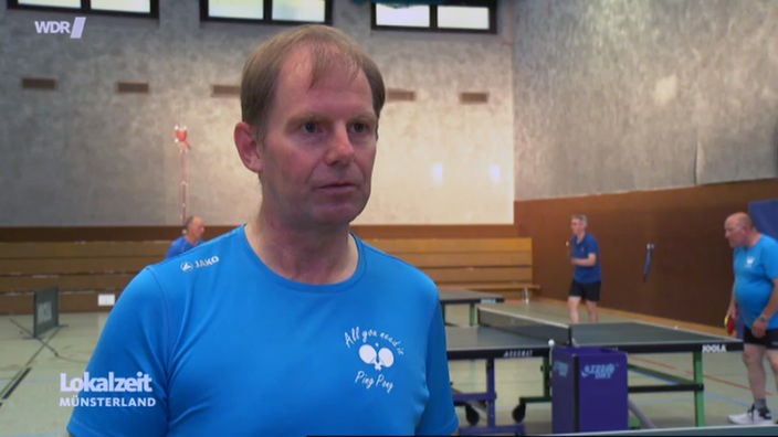 Der Parkinson-Betroffene Stefan Brill steht in einer Sporthalle mit einigen Tischtennisplatten.